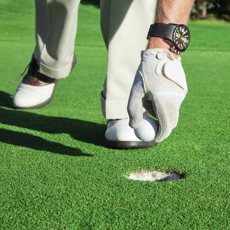 man takes golf ball out of hole laid with fake grass